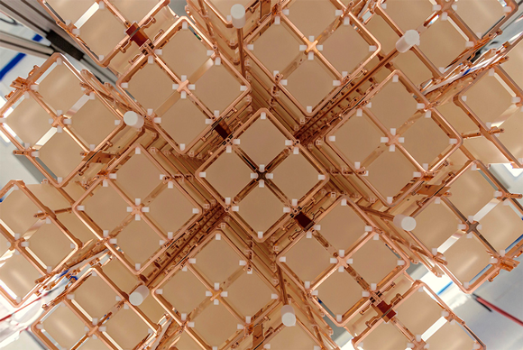 The CUORE detector has 19 copper-framed “towers” that each house a matrix of 52 cube-shaped crystals. Credit: Yury Suvorov/CUORE collaboration Close-up view of an array of cubic, pale crystals held in a copper framework. The structure is composed of multiple repeating units arranged in a symmetrical, grid-like pattern, with small white spacers at the intersections.